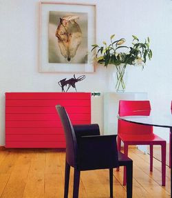Grzejnik płytowy w jaskrawym   czerwonym kolorze krzesła w kontraście z białymi ścianami tworzy wyrazisty element   dekoracyjny salonowego wnętrza
