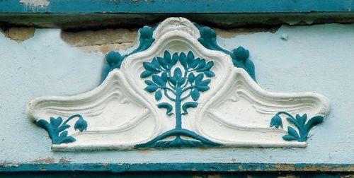 Bardzo czytelny i realistyczny emblemat drzewa nad drzwiami domu. Cały budynek mocno zniszczony, ale płaskorzeźba świeżo odmalowana