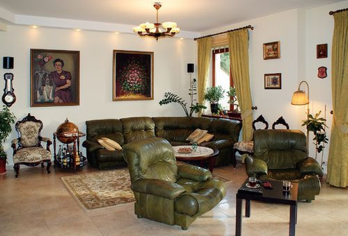 Widok salonu, w którym poczesne miejsce zajmują narożnik i fotele ze skóry w oliwkowym kolorze