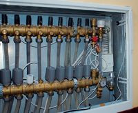 Szafka rozdzielacza z widocznym urządzeniem regulującym przepływy w poszczeg&oacute;lnych pętalach grzewczych