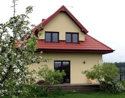 Dach pokryty czerwoną blachodachówką, akrylowy tynk w kolorze jasnożółtym, brązowa stolarka okienna i drzwiowa oraz ceramiczne brązowe wykończenia podmurówki i ganku sprawiają, że dom wygląda tradycyjnie i bardzo przyjaźnie