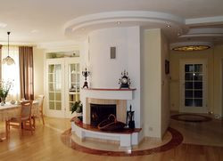 Komunikacja w pomieszczeniach dziennych &#8222;kręci się&#8221; wokół kominka. Ten zabieg architekta wnętrz podkreśla okrągła bryła kominka, wykończona trawertynem w trzech kolorach. Podłogi wykonano z płyt trawertynu oraz z jesionowej deski parkietowej