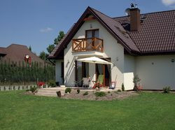 Dom od tyłu. Z powodu wysokiego poziomu wód gruntowych budynek zbudowano o 50 cm wyżej, niż przewidywał projekt i obsypano łagodną skarpą.