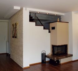 W projekcie nie przewidywano ściany przy narożnym kominku. Można było wokół niego chodzić. Ale właściciele postawili tu ścianę, zyskując schowek pod schodami i większą intymność w salonie. Kominek (bez rozprowadzenia ciepła) wykończono granitem