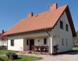 Budynek ma zwartą bryłę i dwuspadowy dach, czyli typowe cechy obniżające koszty budowy. Mury otynkowano tynkiem mineralnym, a dach pokryto ceramiczną dachówką w ceglastym kolorze. Dla oszczędności budowę garażu właścicielka odłożyła na przyszłość. Dziś tego żałuje