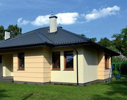 Planując dom na całe życie, Marta i Michał bardzo starannie wybrali projekt. Dom ma zgrabną i zwartą bryłę, ozdobioną dwoma wykuszami w kuchni i w salonie. Dach pokryli szwedzką blachodachówką w grafitowym kolorze. Gładkie fragmenty elewacji pomalowali na jasnożółto, boniowane – na beżowo