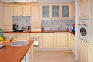 Zabudowa w kuchni w kształcie litery L, z wyspą pośrodku. Na wyspie zlew do mycia produktów, drugi zlew na blacie pod ścianą do mycia garnków