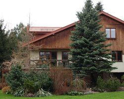 Dom z tyłu. Po rozbudowie ma narożny balkon przy piętrze oraz taras przy głównym wejściu do domu