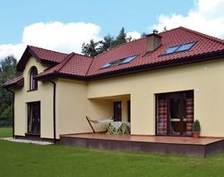 Tył domu zwrócony jest na południowy zachód. To sprawia, że strefa wypoczynkowa na zewnątrz i wewnątrz budynku jest dobrze oświetlona i słoneczna. Mimo tego, właściciele wstawili dodatkowe okna połaciowe nad salonem. Dach z lukarnami wykończyli angobowaną dachówką ceramiczną