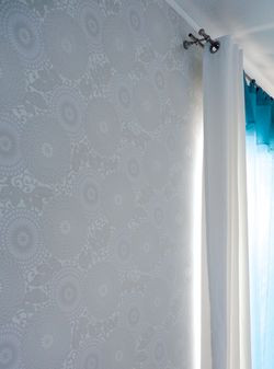 Jedna ze ścian białej sypialni została pokryta białą tapetą o zróżnicowanej strukturze