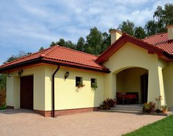 Właściciele chętnie wypoczywają na zadaszonym ganku, bo skierowany jest ku rzadko uczęszczanej, bocznej drodze. Wysunięty garaż osłania go od głównej szosy, dlatego jest na nim cicho i przytulnie. Odpowiednio wyprofilowany podjazd zapewnia odpływ wody sprzed budynku