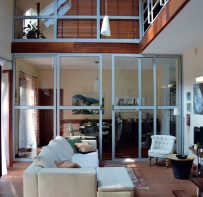 Przeszklenia wewnątrz domu są niemal identyczne, jak w kamienicy włoskiego projektanta Antonio Citterio. Kanapy z duńskiej firmy Bo Concept też znakomicie naśladują jego meble. Na zdjęciu stoją w układzie zimowym, czyli przodem do kominka. W lecie są odwracane o 180 stopni, w stronę lasu