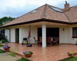 Zaletą domu jest częściowo zadaszony taras o powierzchni 40 m2. Na fragmencie płyty, osłoniętej wysuniętym dachem, latem stoi komplet mebli ogrodowych. Natomiast na nasłonecznionej części płyty podczas upałów rozkłada się basen, chroniąc trawnik przed zniszczeniem