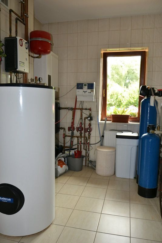Pomieszczenie techniczne zajmuje powierzchnię 8,7 m2. Mieści urządzenia grzewcze, które dobrali pierwsi właściciele domu – m.in. kondensacyjny kocioł na gaz z sieci, wolno stojący zasobnik c.w.u. o poj. 300 l, elementy instalacji solarnej opartej na kolektorach próżniowych. Delfina i Andrzej zamontowali tu natomiast pralkę oraz rozbudowaną stację uzdatniania wody z przydomowej studni z filtrami mechanicznymi, kolumnami pozbawiającymi wodę nadmiaru żelaza i manganu, zmiękczaczem wody