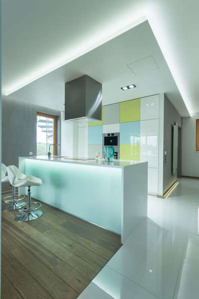 Jasne fronty współgrają z liniowym oświetleniem LED, które wykorzystano wokół podwieszanego sufitu, pod blatem wyspy oraz przy posadzce