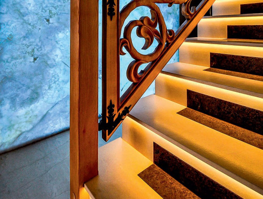 Kamiennym schodom z podświetleniem LED ciepła i stylu dodaje drewniana rzeźbiona balustrada