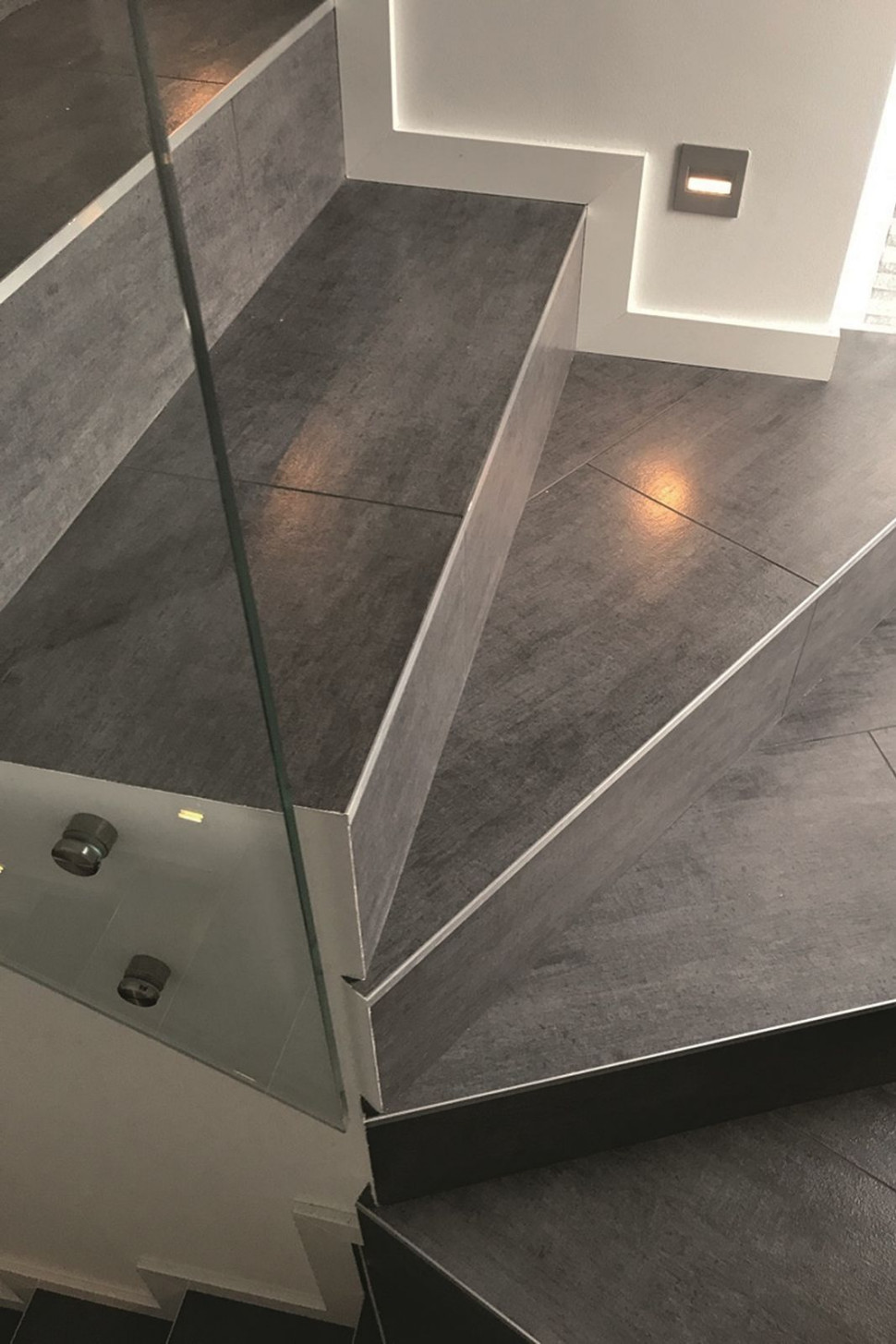 Stopnie i postopnice wykończone płytami gresu, pełna balustrada bez pochwytu wykonana ze szkła osadzonego w stali nierdzewnej