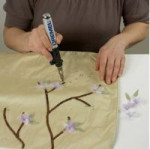 Z zielonej tkaniny wytnij liski i użyj pistoletu do klejenia Dremel Glue Gun do przyklejenia ich na poduszkach