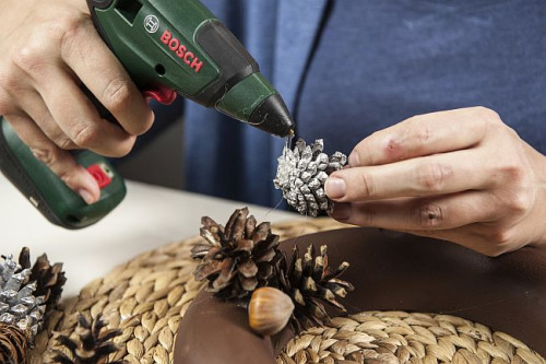 Po wyschnięciu farby, przy pomocy urządzenia do klejenia na gorąco zaczynamy przyklejać szyszki i orzechy