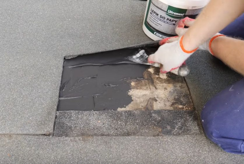 Naprawa pokrycia dachowego z papy przed zimą - Na odkrytą część dachu szpachelką nakładamy lepik, starając się zaaplikować trochę produktu także pod starą papę.