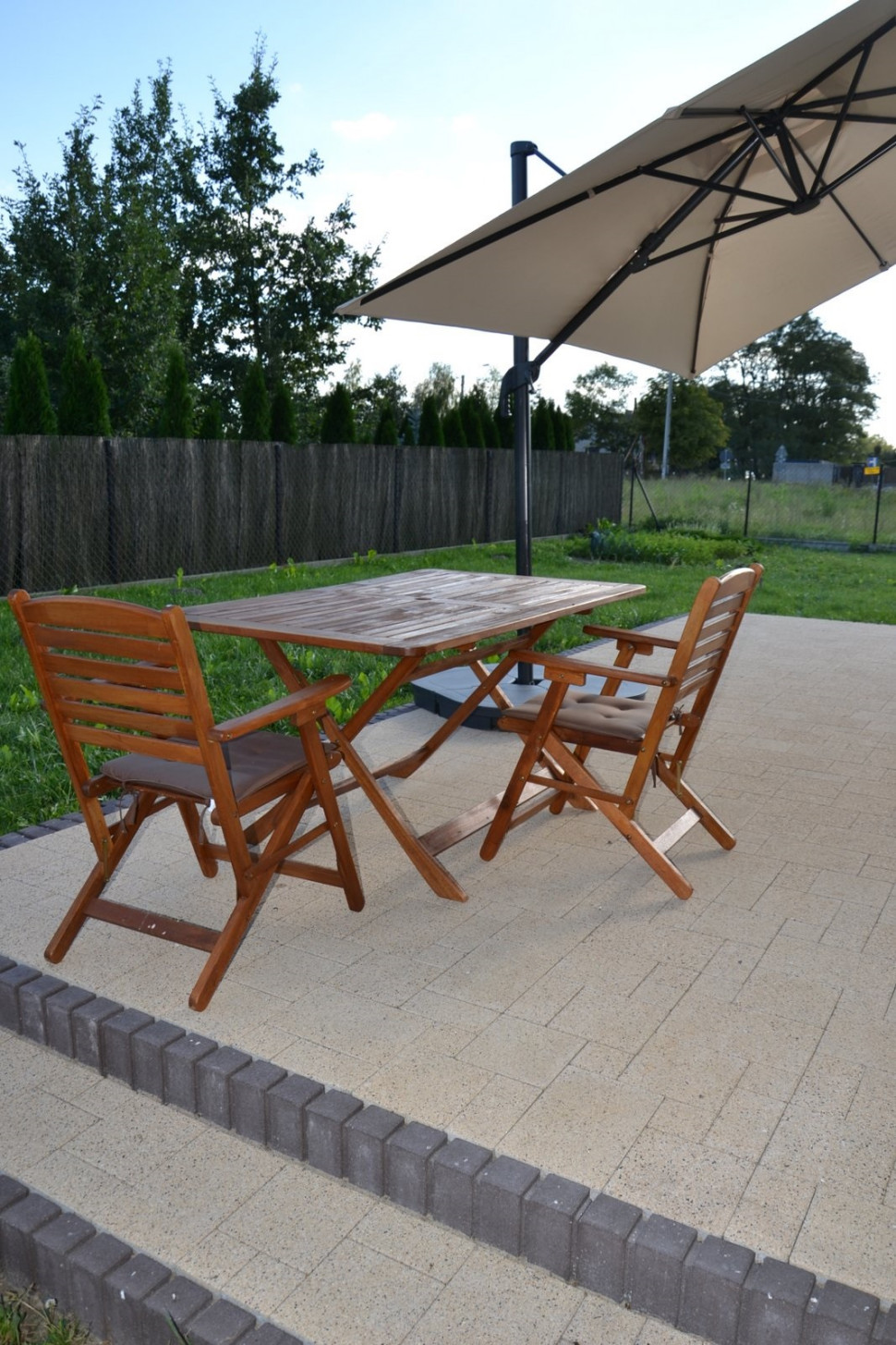 Taras z kostki betonowej zadaszony balkonem i parasolem