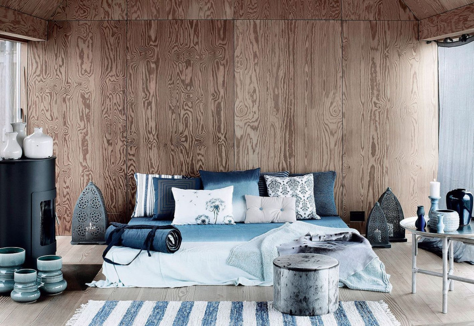 Na zdjęciu drewno schłodzone niebiesko-białą pościelą i ręcznie wykonanym dywanem Lousin marki Broste Copenhagen