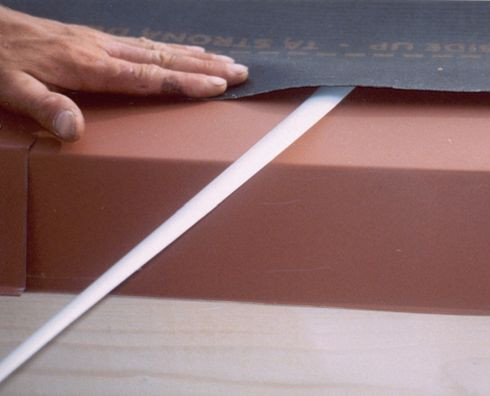 Membrany MWK w wielu wersjach wykonania okapu powinny być przyklejane do obróbek blacharskich. Na tych zdjęciach są nimi kapinosy odprowadzające przecieki i skropliny poza okap. Klejenie najlepiej jest wykonać za pomocą specjalnych taśm dwustronnych. Układamy membranę, a na końcu usuwamy osłonę taśmy i dociskamy do niej membranę.