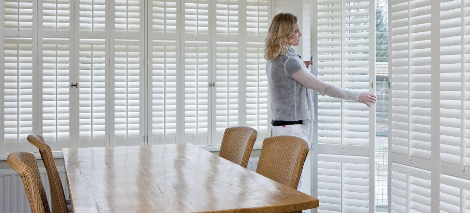 Kobieta otwierająca drewniane okiennice wewnętrzne z ruchomymi lamelami