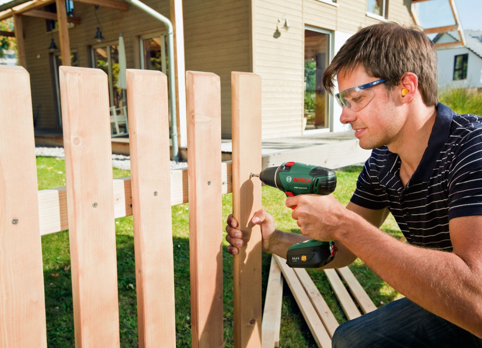 Mężczyzna używa wkrętarki do mocowania płotu