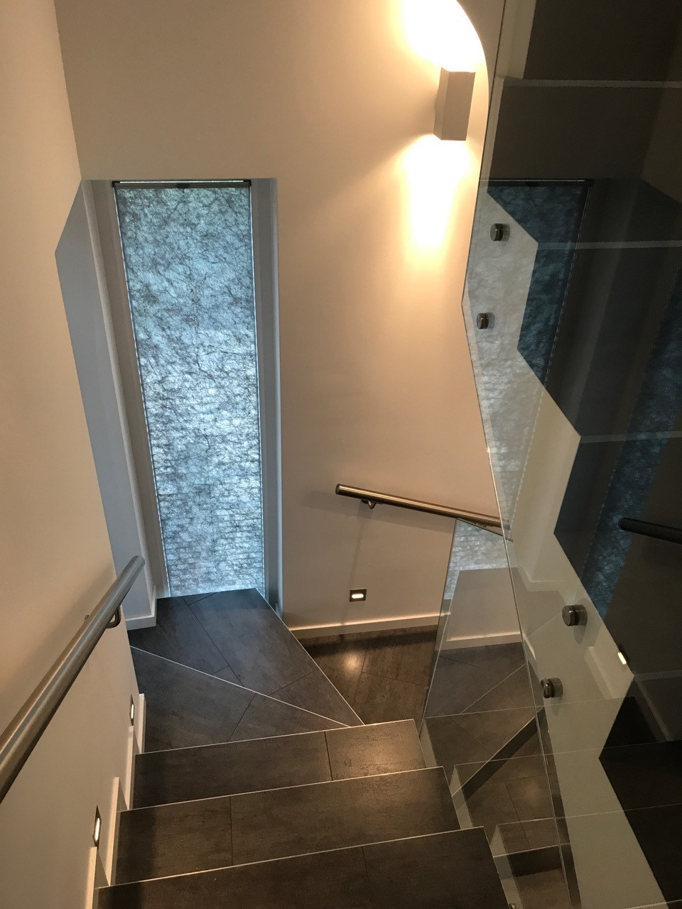 Szklana, pełna balustrada bez pochwytu dodaje lekkości wielokondygnacyjnej klatce schodowej