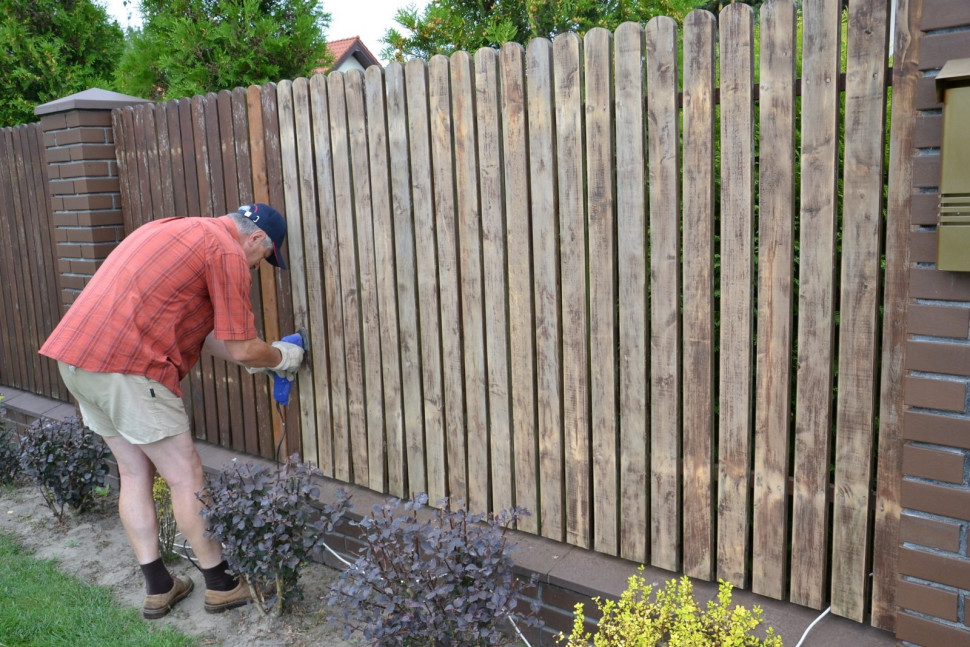 Wzdłuż ulicy stoi ogrodzenie z cegły klinkierowej i sztachet z olchy. Sztachety są właśnie odnawiane