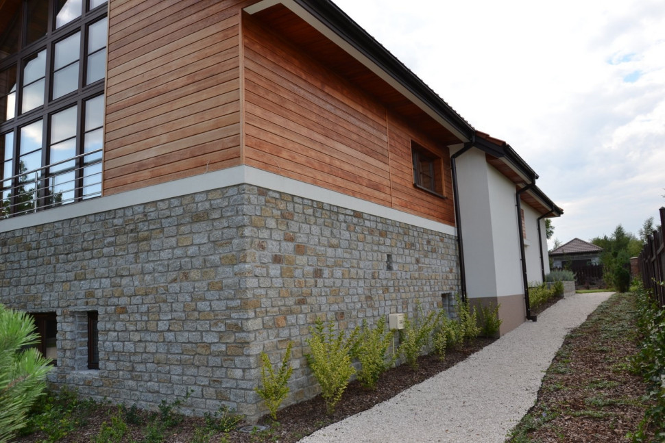 Tylna elewacja jest urozmaicona drewnem, kamieniem i tynkiem silikonowym. Brązowy pas na cokole to marmolit