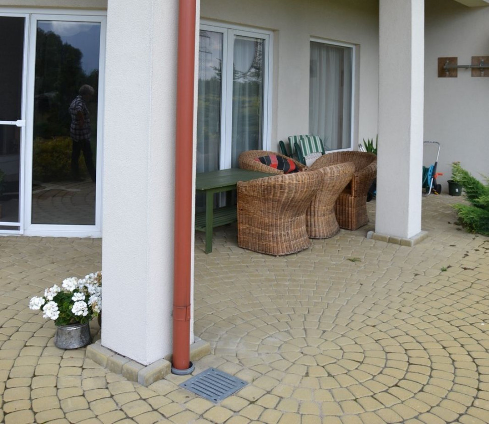 Rura spustowa na tarasie odprowadza deszczówkę poprzez rurę drenującą, ułożoną pod kostką betonową i pod trawnikiem do beczki zakopanej w ogrodzie