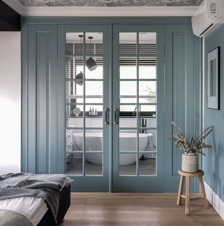 Dwuskrzydłowe przeszkolenie drzwi oddzielające sypialnię od pokoju kąpielowego wykonane z drewna pomalowanego na kolor ściany