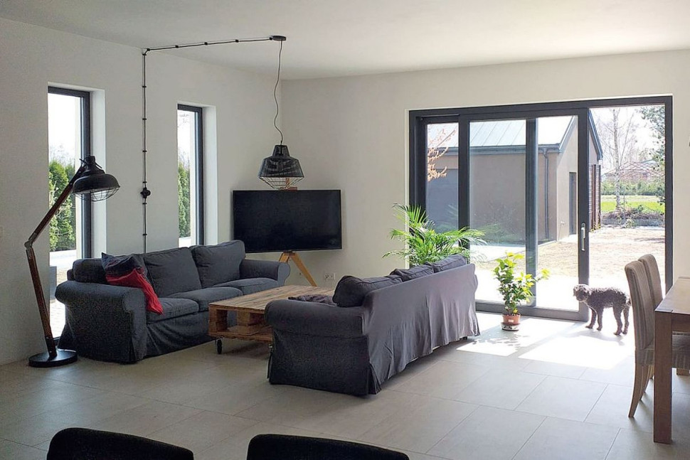 Przestrzeń dzienną optycznie powiększa jednolita posadzka, wykończona szarymi płytami gresu imitującymi beton