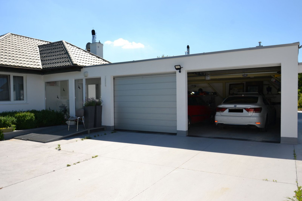 Do istniejącego parterowego domu, przykrytego kopertowym dachem, dobudowano łącznik i garaż na dwa samochody, wykończone dachem płaskim, schowanym za attyką