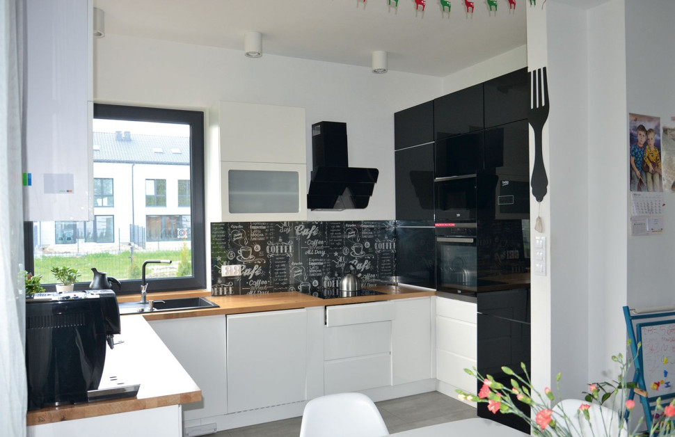 Kuchnia wyposażona w pojemną zabudowę systemową z płyty MDF, polakierowana na biało i czarno, blat roboczy z drewna bukowego