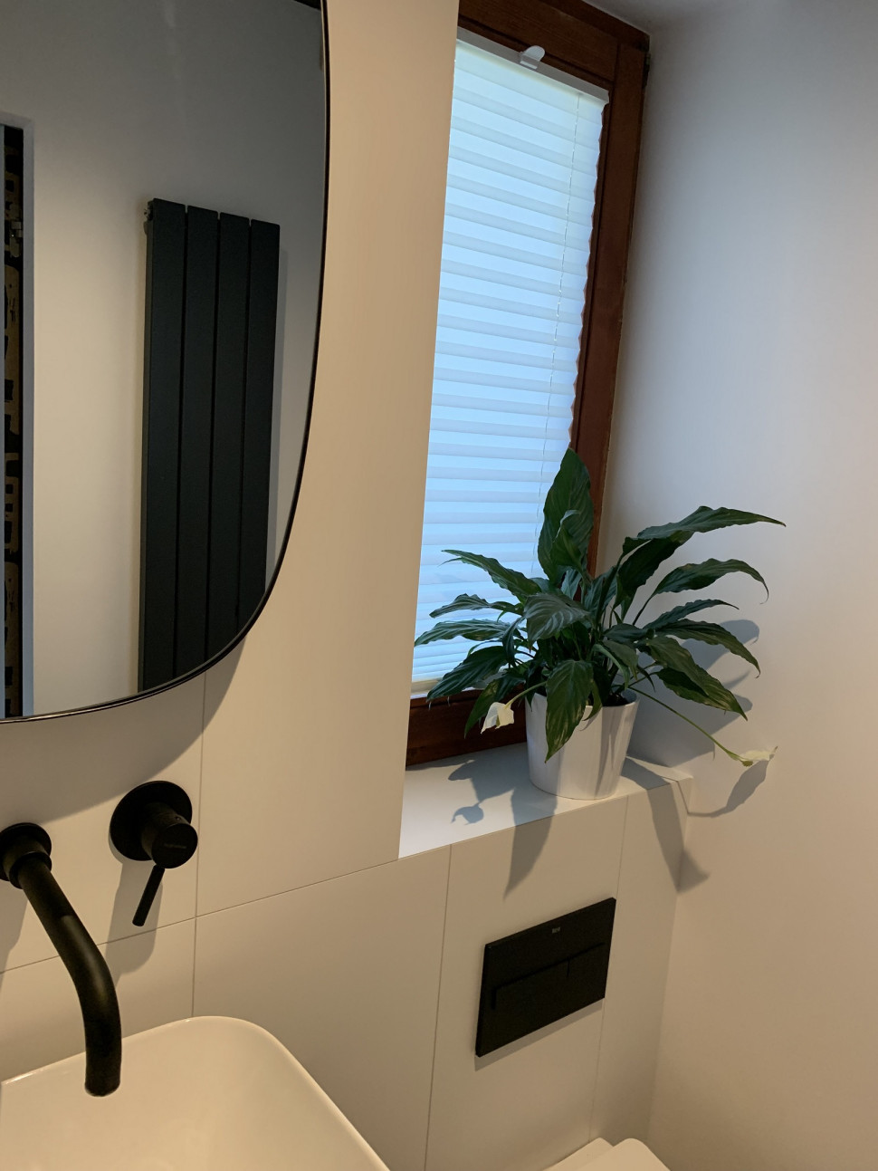 Czarny podtynkowy osprzęt i długi wąski grzejnik dekoracyjny (pokazuje go odbicie w lustrze)