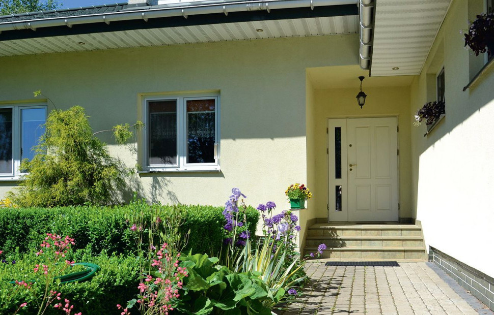 Główne wejście do domu zamknięto bezpiecznymi drewnianymi drzwiami z przeszklonym bocznym doświetlem