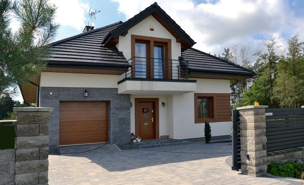 Dwukondygnacyjny dom ma zwartą bryłę, która obejmuje garaż na 1 samochód