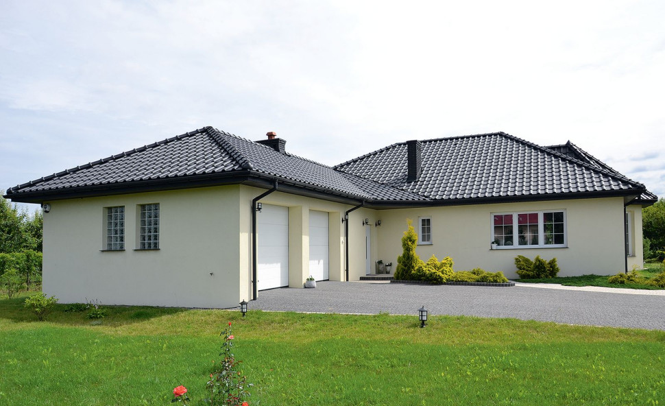 Parterowy dom rozciąga się na planie litery T, a rozłożystą bryłę przykrywa wielospadowy dach z ceramiczną dachówką