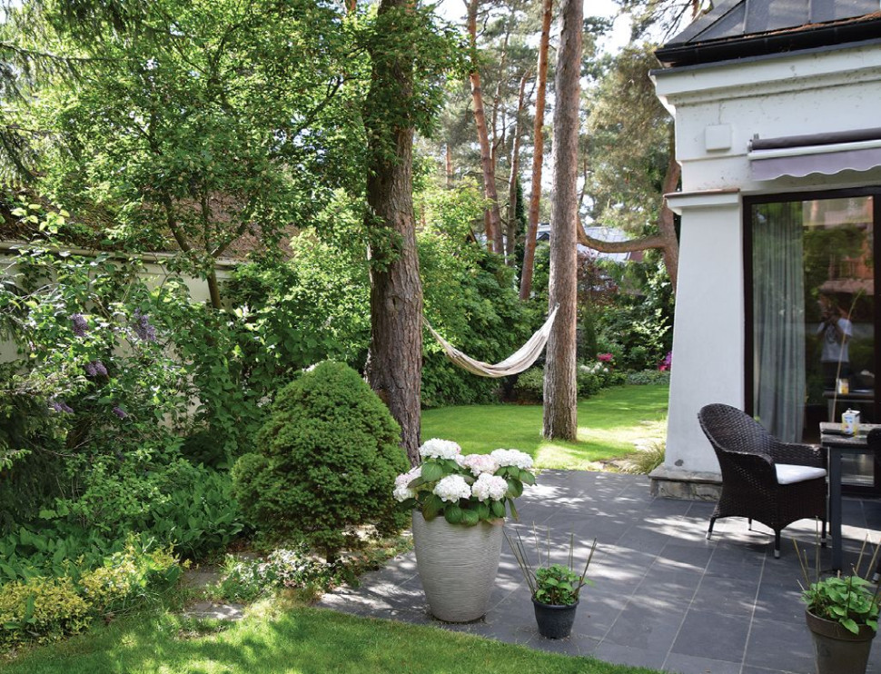 Zakątek z hamakiem, urządzony przy strefie z ogrodem zimowym i tarasem z kamienną posadzką