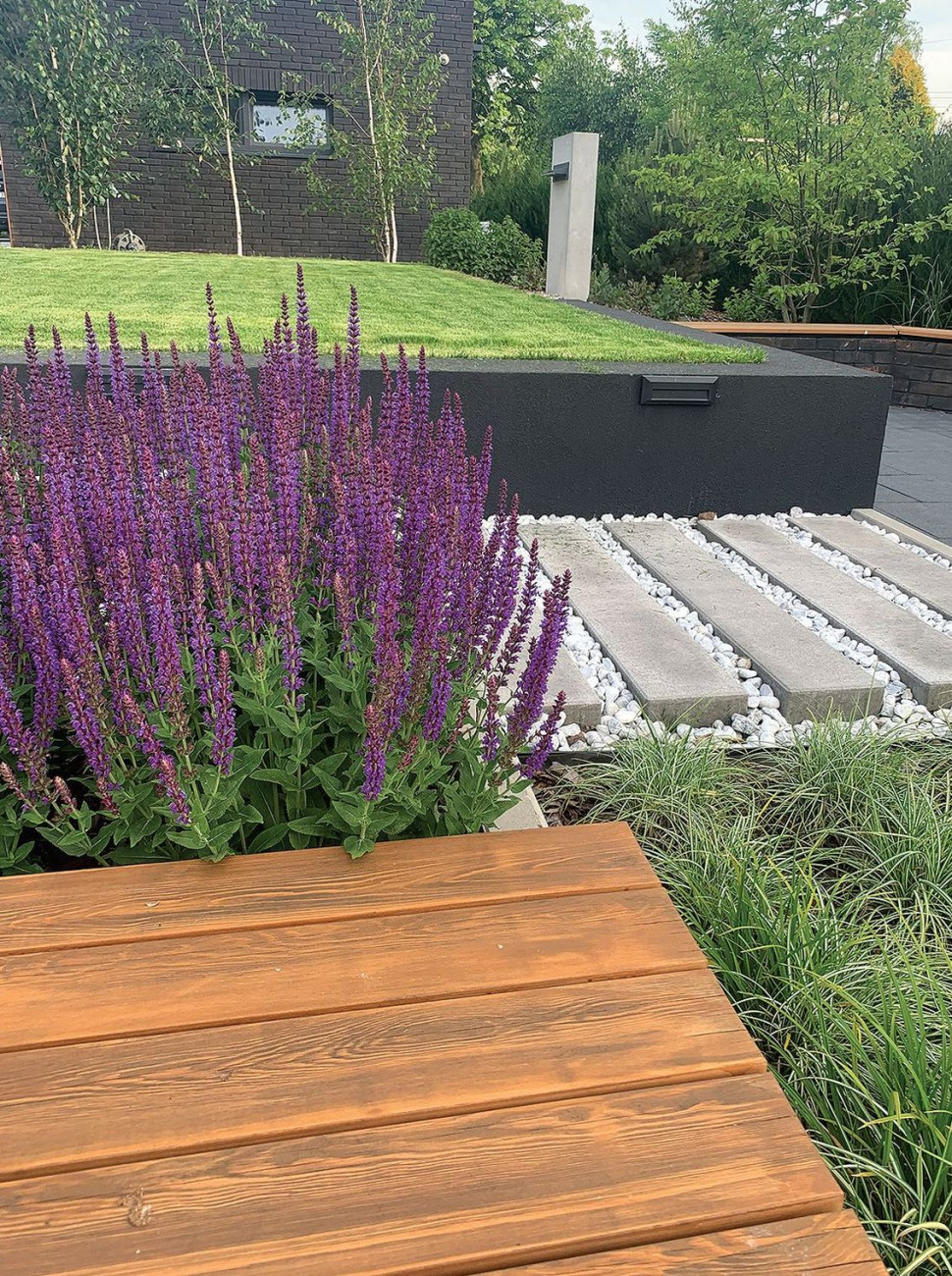 Ogród Natalii i Michała wyróżnia się kaskadowym rozplanowaniem trawników, murków i donic o różnych rozmiarach, powtórzeniem materiałów i kolorystyki na elewacji oraz podkreśleniem detali architektonicznych minimalistyczną szatą roślinną i urozmaiconym oświetleniem