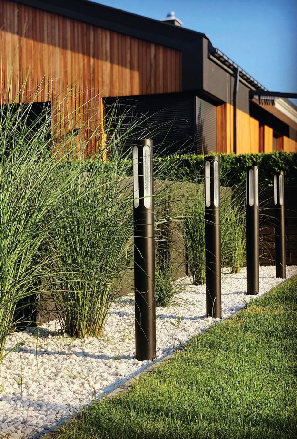 Do zakątka z okazałymi trawami projektantka dobrała wysokie lampy-słupki