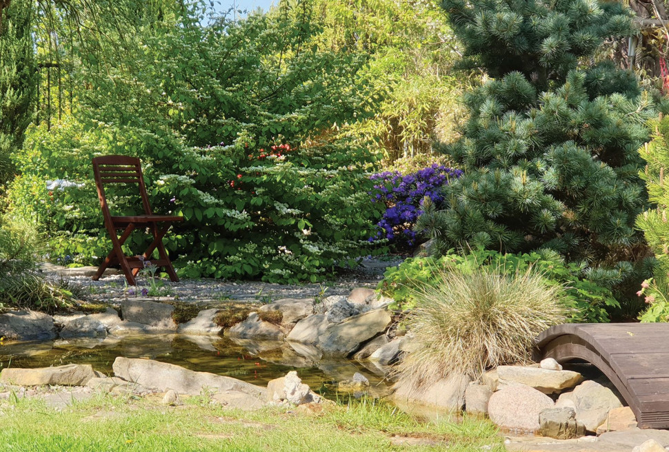 W centrum ogrodu rozciąga się głębokie do 1,5 m oczko wodne, przez które projektantka przerzuciła japoński mostek o łukowatym kształcie