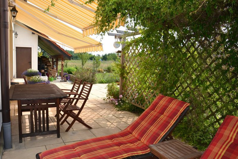 Narożny taras zadaszony jest dwoma markizami oraz drewnianą pergolą z pnączami