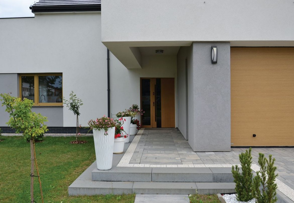 Szerokie przeszklone wejście do budynku ulokowano pod długim podcieniem