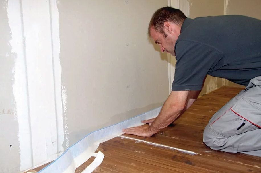 Płytki ceramiczne na parkiecie - krok 1) Przyklejenie elastycznej taśmy - dwustronnie pokrytej specjalną powłoką z flizeliny - do uszczelnienia szczelin dylatacyjnych i naroży