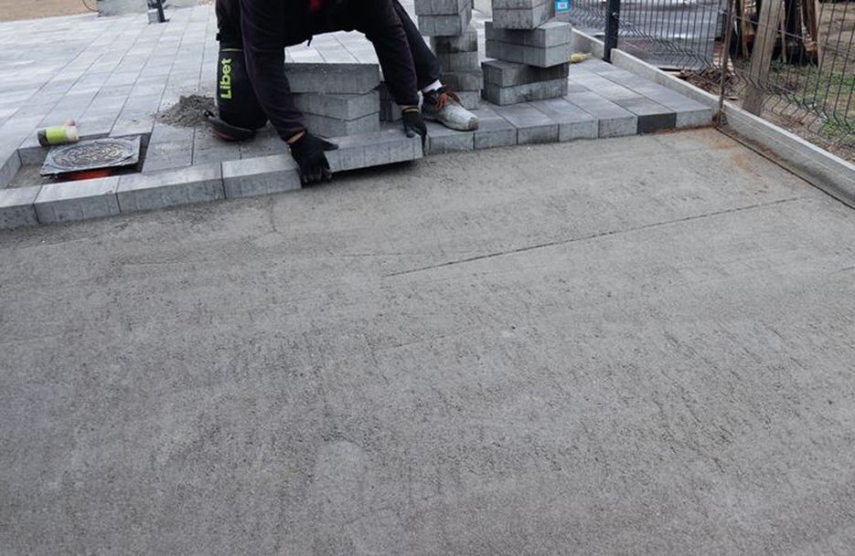 Wyrównywanie warstwy spadkowej długą łatą murarską i układanie kostki