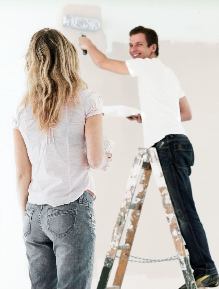 Mężczyzna maluje ścianę wałkiem stojąc na drabinie